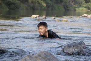 Asian boys are spending their freetimes by diving, swimming, throwing rocks and catching fish in the river together happily. Hobby and happiness of children concept. photo