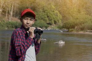 Asian boys using binoculars to watch birds on trees and fish in river in local national park during summer camp, idea for learning creatures and wildlife animals and insects outside the classroom. photo