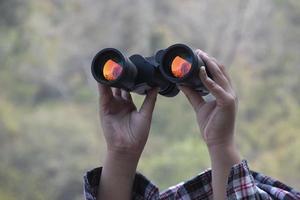 Hands holding binoculars, blurred natural background, concept for vacation, observation, trekking, camping, hiking and birdwatching. photo