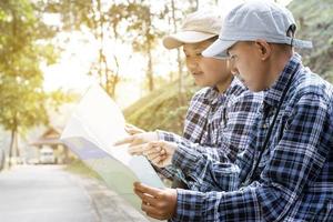 Asian young teen boys hold national park map, reading details of birdwatching before using their binoculars to watch the bird which sitting on brunches and flying in the sky, summer vacation concept. photo