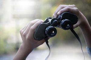 Hands holding binoculars, blurred natural background, concept for vacation, observation, trekking, camping, hiking and birdwatching. photo