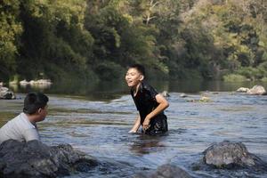 Asian boys are spending their freetimes by diving, swimming, throwing rocks and catching fish in the river together happily. Hobby and happiness of children concept. photo