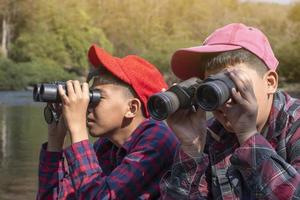 Asian boys are using binoculars to watch birds and fish  in local national park during summer camp, idea for learning creatures and wildlife animals and insects outside the classroom. photo