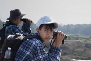 Asian boys are using binoculars to watch birds and fish  in local national park during summer camp, idea for learning creatures and wildlife animals and insects outside the classroom. photo