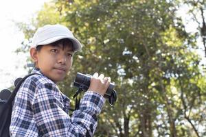 Asian boys using binoculars to watch birds on trees and fish in river in local national park during summer camp, idea for learning creatures and wildlife animals and insects outside the classroom. photo