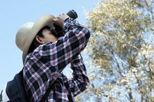 Asian boys using binoculars to watch birds on trees and fish in river in local national park during summer camp, idea for learning creatures and wildlife animals and insects outside the classroom. photo