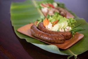 Delicious grilled herbed pork sausage from the barbecue served in the restaurant. Close-up shot of Thai sausage with fresh vegetable side dish, Thai food photo
