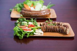 Delicious grilled herbed pork sausage from the barbecue served in the restaurant. Close-up shot of Thai sausage with fresh vegetable side dish, Thai food photo
