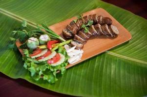 Delicious grilled herbed pork sausage from the barbecue served in the restaurant. Close-up shot of Thai sausage with fresh vegetable side dish, Thai food photo