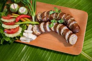 Delicious grilled herbed pork sausage from the barbecue served in the restaurant. Close-up shot of Thai sausage with fresh vegetable side dish, Thai food photo