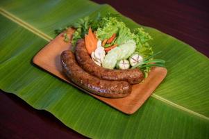 Delicious grilled herbed pork sausage from the barbecue served in the restaurant. Close-up shot of Thai sausage with fresh vegetable side dish, Thai food photo