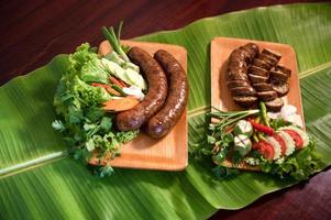 Delicious grilled herbed pork sausage from the barbecue served in the restaurant. Close-up shot of Thai sausage with fresh vegetable side dish, Thai food photo