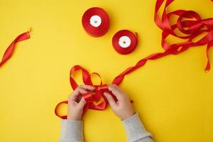 two female hands tie a bow with a red ribbon and reels with a satin ribbon photo