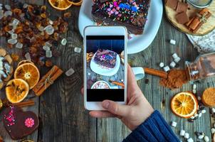 White smartphone in a woman's hand takes a piece of cake and sweets photo