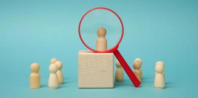 wooden figures of men stand on a beige background and a plastic magnifying glass. Recruitment concept, search for talented and capable employees photo