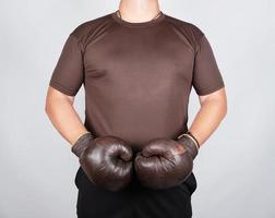 young man stands wearing very old vintage brown boxing gloves on his hands, white background photo
