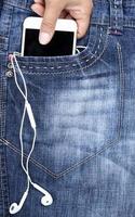 la mano pone un teléfono inteligente blanco en el bolsillo delantero de los jeans azules foto