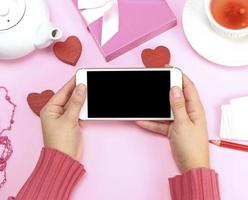 dos manos femeninas en un suéter rosa sosteniendo un teléfono inteligente blanco foto
