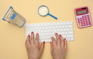 female hands and white wireless keyboard, stack of paper receipts and magnifier on yellow background photo