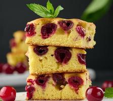 trozos horneados de bizcocho con cerezas maduras rojas sobre una tabla de madera blanca foto