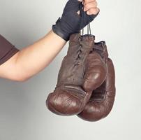 el brazo de los hombres envuelto en una venda deportiva elástica negra sostiene un par de guantes de boxeo de cuero antiguos foto