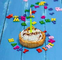 sweet cake with white cream and a burning yellow candle photo