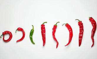 whole ripe red hot chili peppers on a white background, one green photo