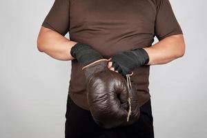 man stands and puts on his hands very old vintage brown boxing gloves photo