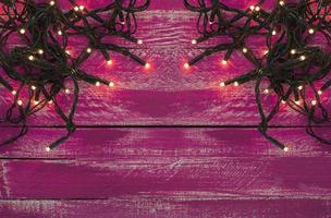 Christmas garland with small light bulbs on the pink shabby wooden surface photo