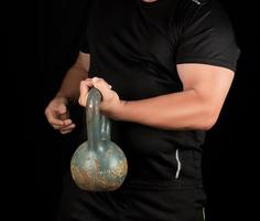 adult strong athlete in black clothes holding an iron kettlebell photo