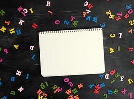 pequeñas letras de madera multicolores del alfabeto inglés y cuaderno de papel foto