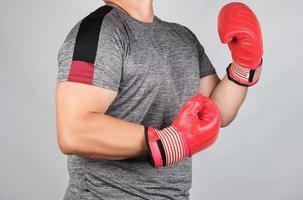 muscular adult athlete in gray uniform and red leather boxing gloves standing in a rack photo