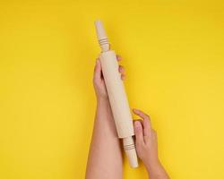 hand holding a wooden rolling pin on a yellow background photo