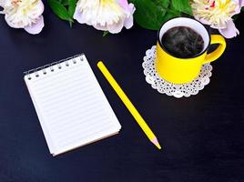 cuaderno vacío y taza amarilla con café caliente foto