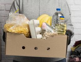 mujer en un suéter gris está empacando comida en una caja de cartón, el concepto de asistencia y voluntariado foto