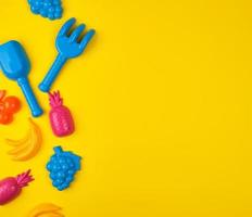 multicolored plastic toys fruits on a yellow  background, copy space photo