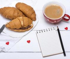 taza de cerámica roja con café caliente y croissants recién hechos foto