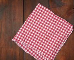 toalla de cocina a cuadros rojos blancos sobre un fondo de madera marrón foto