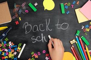 female hand writes with a white chalk on a blackboard back to school photo