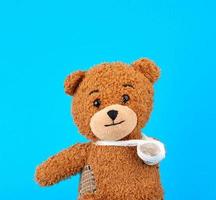 brown teddy bear with a bandaged paw sitting on a blue background photo