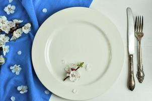 plato blanco y cubiertos, cerca de una rama de flor de cerezo foto