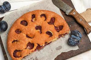 half sponge plum cake on parchment paper and knife, top view photo