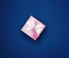 square closed pink box with white bow on a blue background, top view photo