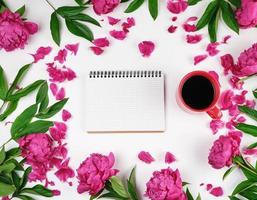 open notebook in a cage and a red cup of coffee on a white background photo