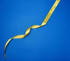 yellow silk thin ribbon twisted on a blue background, trendy classic color photo