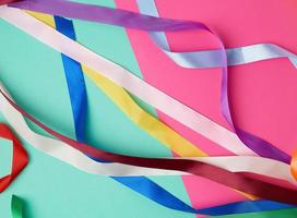 many silk multi-colored ribbons on a colored background photo