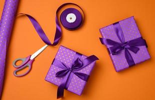 cajas de regalo atadas con cinta de seda púrpura sobre un fondo naranja, vista superior. telón de fondo festivo foto