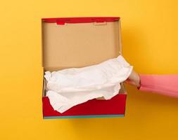 mano femenina sosteniendo una caja de cartón roja abierta sobre un fondo amarillo, entrega foto