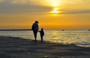 Silhouette of a woman with a child, they hold hands on a background of sea sunset photo