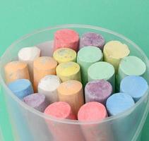 multicolored chalk in a plastic bucket on a green background, photo